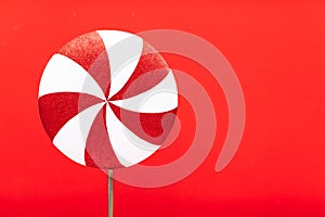 Red-white lollipop swirl on a white stick over red background. Top view, copy space. huge red and white candy. Sweetness