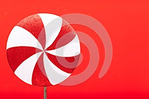 Red-white lollipop swirl on a white stick over red background. Top view, copy space. huge red and white candy. Sweetness