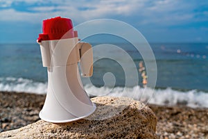 Red and White loudspeaker or horn megaphone for important public information against blue sea at beach