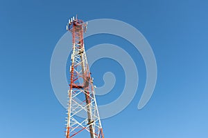A red and white mobile or cell phone telecommunications tower on a blue sky background looking up