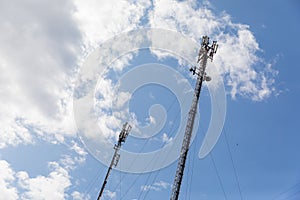 Red and white mobile phone cell tower repeater, with a small microwave dish on blue sky with clouds background