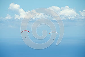 Red and white paragliders fly over Indian ocean with clouds at the background in Reunion island, France.