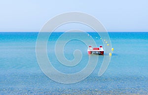 Red and white pedalo on a calm blue sea, near yellow buoys