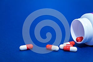 Red and white pill capsules poured from a white plastic bottle container. Global healthcare concept on blue background.