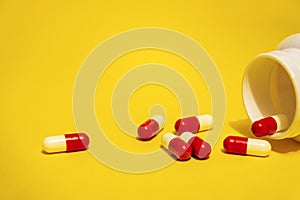 Red and white pill capsules poured from a white plastic bottle container. Global healthcare concept on yellow background.