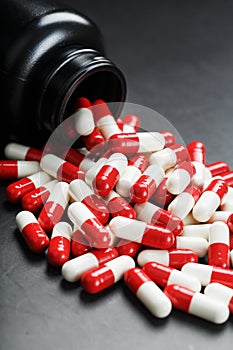 Red and white pills from a black jar on a black background.