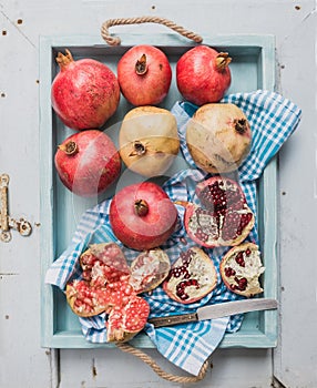 Red and white pomegranates with knife on kitchen towel in blue tray over light painted wooden backdrop