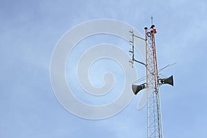 The red and white radio transmitter is equipped with loudspeaker and red light. On a bright sky background