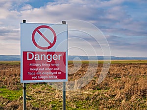 A red and white sign in English warns the public to keep out of land designated for use as a military firing range.