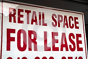 A red and white sign saying retail space for lease with border hangs in a vacant storefront glass window in Chicago during the