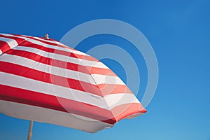 Red and white striped beach umbrella against blue sky, space for text