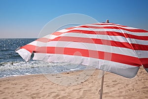 Red and white striped beach umbrella on sandy seashore