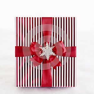 Red and white striped Christmas gift present with metallic wrapping paper, satin ribbon bow and silver glitter snowflake