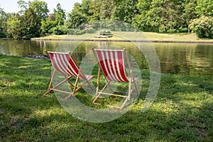 Red and white striped sun loungers standing in the lawn on the natural bank of a river, inviting idyll on a sunny summer day, copy