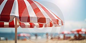 Close up of red and white striped sun parasol with blurry beach on sunny day in background