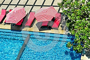 Red and white striped umbrellas next to matching loungers by a vibrant blue pool