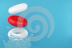Red and white swimming rubber rings on blue background with water splashes. A splash of water. Floating lifebuoy.