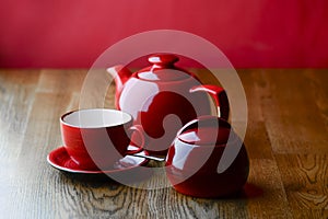 Red and white tea set with on dark wooden table with hot pink background.