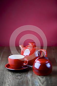 Red and white tea set with on dark wooden table with hot pink background.