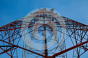 Red white telecommunication tower against blue sky - bottom view