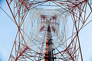 Red white telecommunication tower against blue sky - bottom view