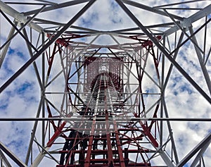 Red white telecommunication tower against blue sky and white cloud- bottom view