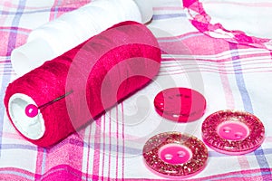 Red and white thread and buttons on a checkered cloth. Sewing accessories