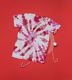Red and white tie dye T-shirt and red and white candy on a red background. Flat lay