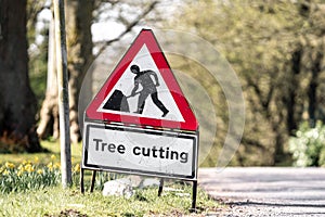 Red and white tree cutting warning sign standing at side of road with road works worker symbol. Traffic sign alerting drivers.