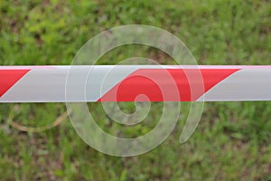 Red and white warning tape stretched on a green grass blurred background.