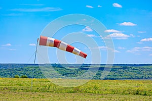Red and white windsock indicating wind direction in open field on clear day