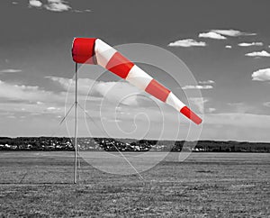 Red and white windsock wind sock  on the aerodrome, monochrome black and white field, sky and clouds background