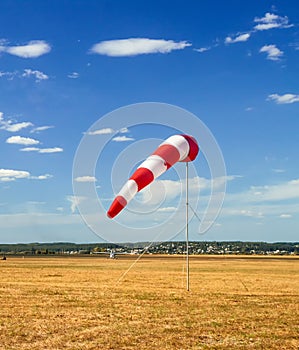 Red and white windsock wind sock on blue sky on the aerodrome, yellow field and clouds background in autumn