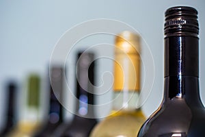 Red and white wine bottles on light background. Focus on the red wine bottle in the foreground