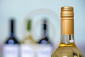 Red and white wine bottles on light background. Focus on the white wine bottle in the foreground