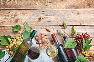 Red and white wine glasses and bottles on wooden background, copy space. Fresh grapes and grape leaves as decoration
