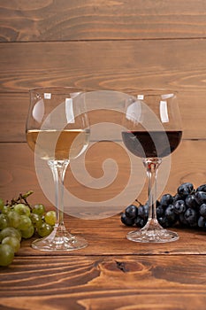 Red and white wine glasses and grape on wooden table