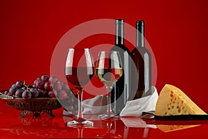 Red and white wine, grapes and cheese on a red background