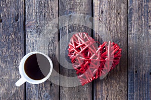 Red wicker heart for Valentine`s day and a white cup with tea or coffee on a wooden table. View from above.