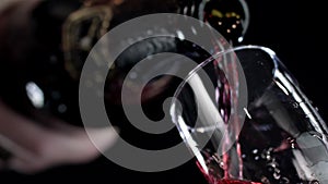 Red wine being poured into a glass of black background. Slow motion