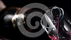 Red wine being poured into a glass of black background. Slow motion