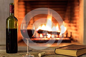 Red wine and a book on burning fireplace background