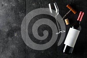 Red wine bottle with corkscrew, cork and wine glass on dark wooden table flat lay from above