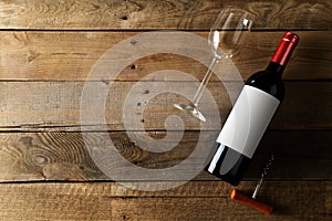 Red wine bottle with corkscrew and wine glass on brown rustic wooden table flat lay from above