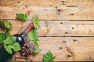 Red wine bottle and fresh grapes on wooden background, copy space