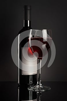 Red wine bottle and full wineglass on black