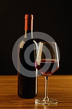 Red wine bottle with glass on black background