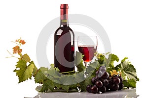 Red wine bottle and glass with grapes and leaves on white background