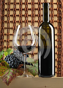 Red wine bottle, glass, grapes, wicker background photo