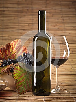 Red wine bottle, glass, grapes, wicker background